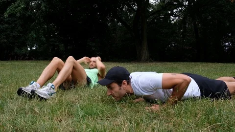 Handheld shot of two young men in sportswear exercising on grass Stock Footage 114879619