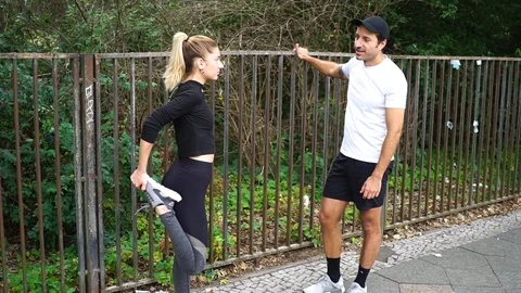 Handheld shot of two young people talking while stretching on the sidewalk Stock Footage 114884542