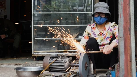 Handheld shot of vietnamese man with face mask working on knife blade on ground Stock Footage 147372279