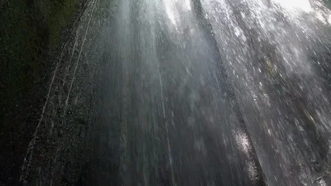 Handheld shot of waterfall with tree branches and sun entering dark cave, Bali Stock Footage 140249404