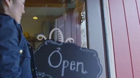 Handheld shot of woman hanging open sign on door at garden center Stock Footage