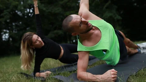 Handheld shot of young couple doing side plank on yoga mat in park Video stock 120429856