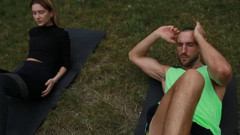 Handheld shot of young couple doing various exercise on yoga mat in park 스톡 동영상 120431589