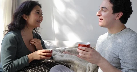 Handheld shot of young couple drinking coffee and talking while sitting on sofa Stock Footage 120427446