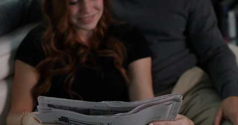 Handheld shot of young couple reading newspaper together while sitting on sofa Stock Footage 119837522