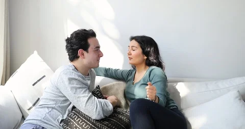 Handheld shot of young couple talking and smiling while sitting on sofa Stock Footage 120425546
