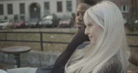 Handheld shot of young couple talking and laughing while sitting on park bench Stock Footage 120434052