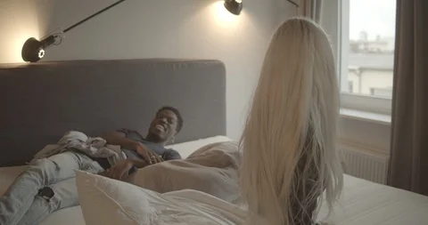 Handheld shot of young couple talking and playing with pillow on bed at home Stock Footage 120435932
