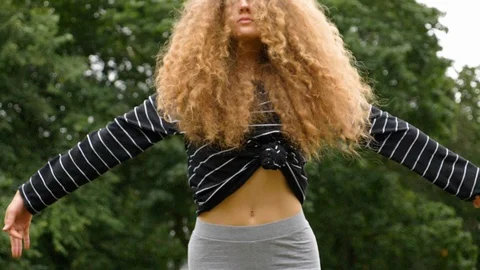 Handheld shot of young curly haired woman stretching in park in slow motion Video stock 114873786
