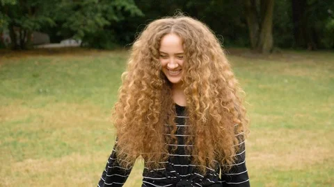 Handheld shot of young curly haired woman laughing in park in slow motion Video stock 114873945