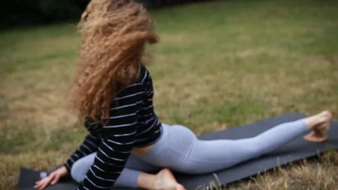 Handheld shot of young curly haired woman doing yoga in park Stock Footage 120428407