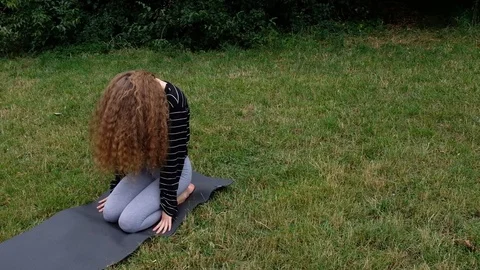 Handheld shot of young curly haired woman stretching while doing yoga in park 스톡 동영상 120434431