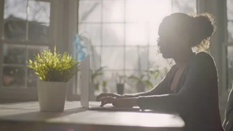 Handheld shot of young lady working from home in slow motion with sun flare 動画素材 151619247