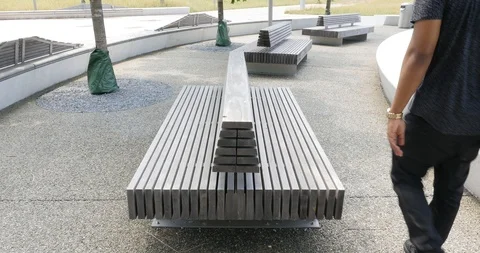 Handheld shot of young man with backpack sitting down on park bench Stock Footage 120147388