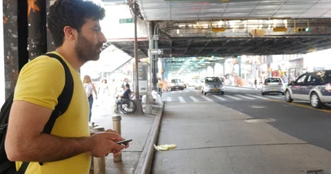 Handheld shot of young man with backpack using smartphone on sidewalk Stock Footage 120150191