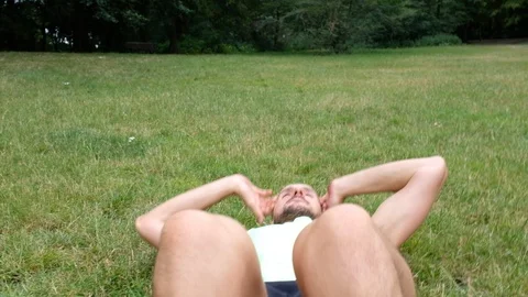 Handheld shot of young man doing sit-ups on lawn Vídeo Stock 120425392