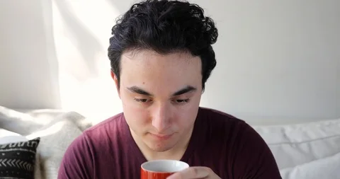 Handheld shot of young man drinking coffee on sofa in living room Stock Footage 120430384