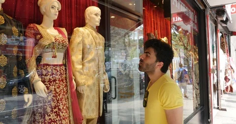 Handheld shot of young man looking at traditional clothes through window display Stock Footage 120064383