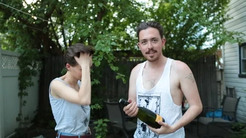Handheld shot of young man opening champagne bottle watched by his girlfriend Stock Footage 114862440