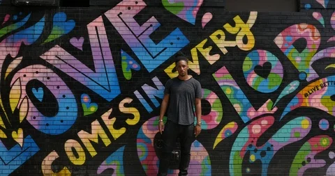 Handheld shot of young man standing against wall with colourful graffiti Stock Footage 120147950