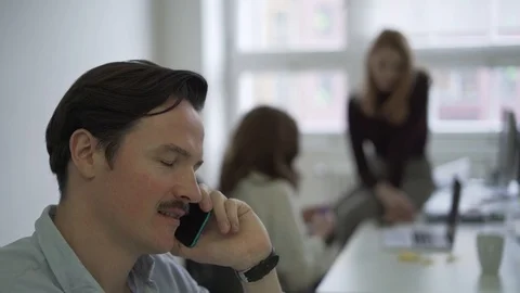 Handheld shot of young man talking over phone and young women working on laptop Stock Footage 114878019