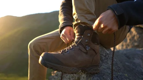 Handheld shot of a young man tying laces of hiking boots while sitting Stock Footage 114881366