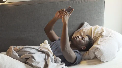 Handheld shot of young man using smart phone while lying on bed at home Vídeo Stock 120433721