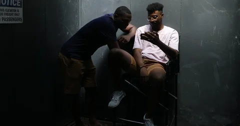 Handheld shot of young men talking while looking at smartphone against wall Stock Footage 120063313