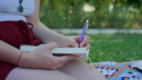 Handheld Side View of Female Hand Writing in Diary on Grass Stock Footage 315800169