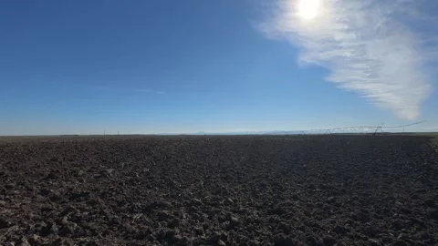 Handheld slow motion over plowed field with irrigation line under blue sky Stockbeeldmateriaal 333286230