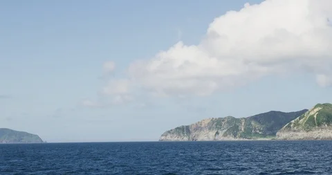 Handheld slow motion shot of blue sea, mountains and sky in background, Japan Stock Footage 124716223