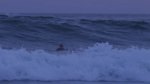 Handheld slow motion shot of young adult man surfing in dark sea after sunset Stock Footage 120285653