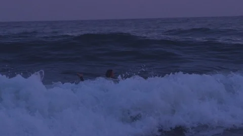Handheld slow motion shot of a young adult surfing in dark sea after sunset Stock Footage 120285731