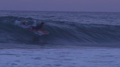 Handheld slow motion shot of a young adult surfing in dark sea after sunset Stock Footage 120286442
