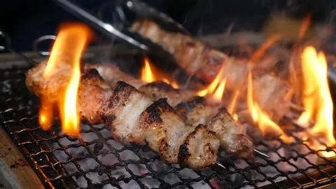 Handheld, slow motion of smoky pork belly skewers turning on hibachi grill Stock Footage