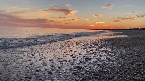 Handheld sunset shot of waves rolling in slow motion towards a beach Stock Footage 166816384