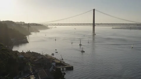 Handheld sunset view of 25 de Abril Bridge and boats sailing over Tagus River Stock Footage 267249532