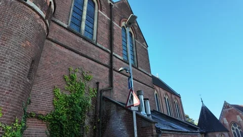 Handheld tracking past brick church facade in London with ivy and road sign Stock Footage 346676951