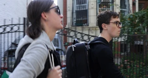Handheld tracking shot of young couple walking along sidewalk on street Stock Footage 120434566