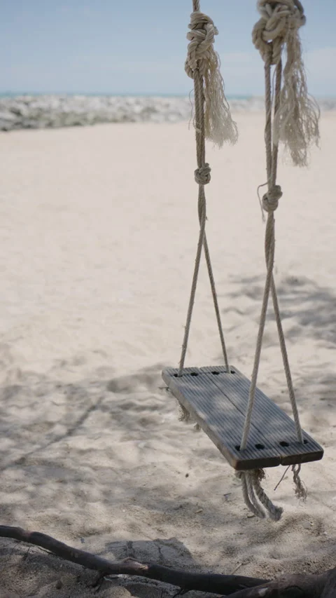 Handheld vertical video of an empty swing swinging on the beach Stock Footage 338242215