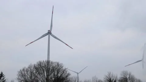 Handheld video of windmills turning in the wind above the trees Stock Footage 169240310