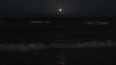 Handheld view of full moon over rough sea at night with boats, moonlight Vídeos de archivo 346708064