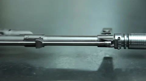 Handheld view moving along the barrel of a rifle, over to three rounds of ammo. Stock Footage 64092634