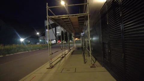Handheld walking POV through a scaffold tunnel over a night sidewalk Stock Footage 345996087