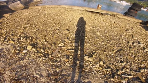 Handhold still view of a extruded cast shadow on to dirt rocky sandy beach groun Stock-Footage 258443402