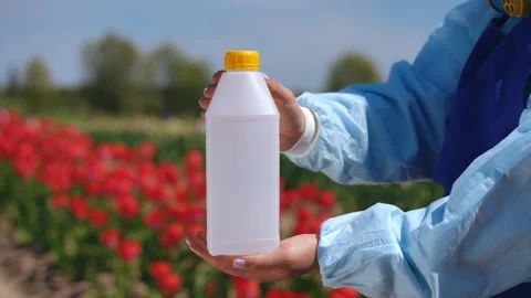 Handholding a transparent bottle while standing amidst a colorful flower field Stock Footage 306839011