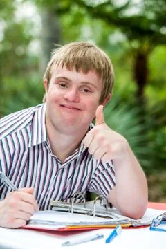 Handicapped boy doing thumbs up at desk outdoors. Stock Photos