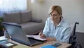 Handicapped grandmother making notes during online lesson home, senior student 4k or 4k+ Resolution