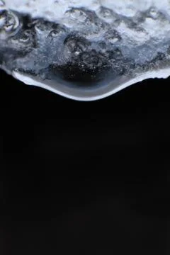 Handing down water drop from ice top. Cold clear rain drop with ice reflectio Stock Photos