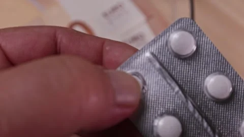Handling a pill blister pack while preparing to take medication with a stack of Vidéo 320127081
